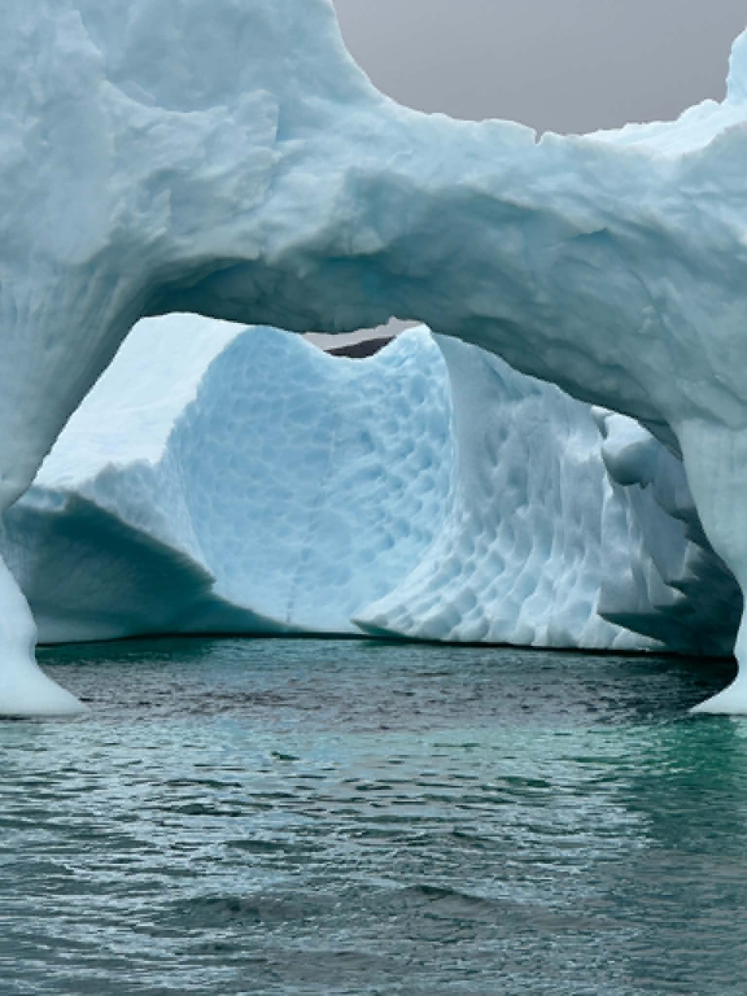 A natural arch in a glowing blue iceberg with calm water beneath