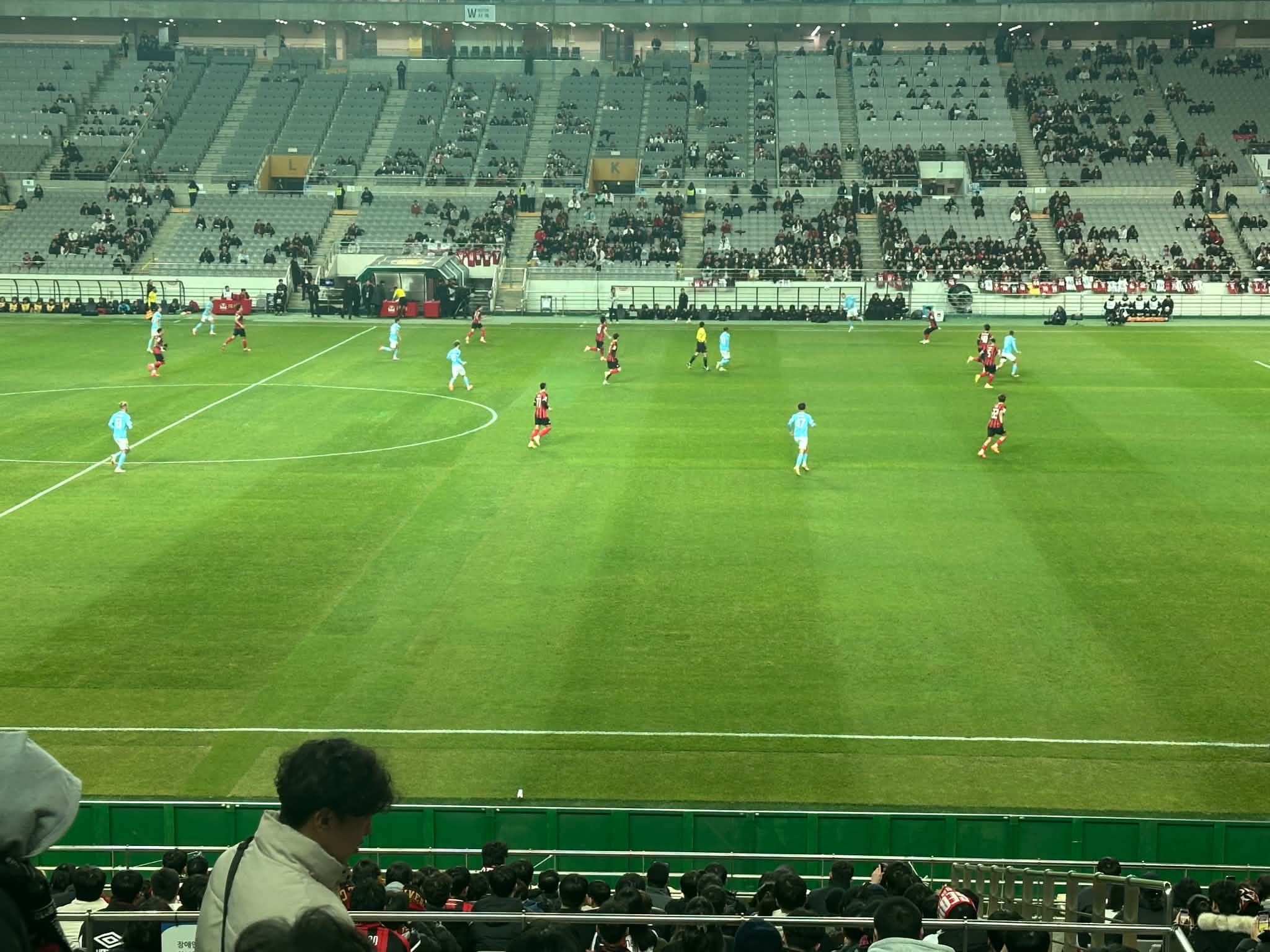 FC Seoul (red and black kit) playing Melbourne (cyan) at Seoul World Cup Stadium, with a small foreground crowd and empty upper stands behind