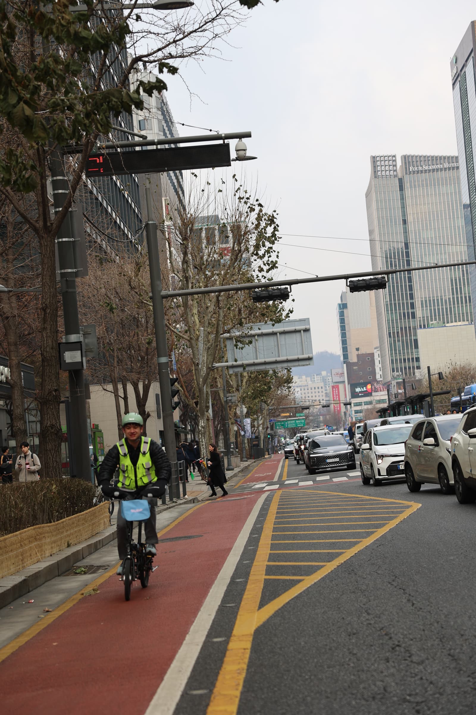Anthony on the bike tour wearing a hi-vis vest on a red bike lane in Seoul, with modern buildings in the background
