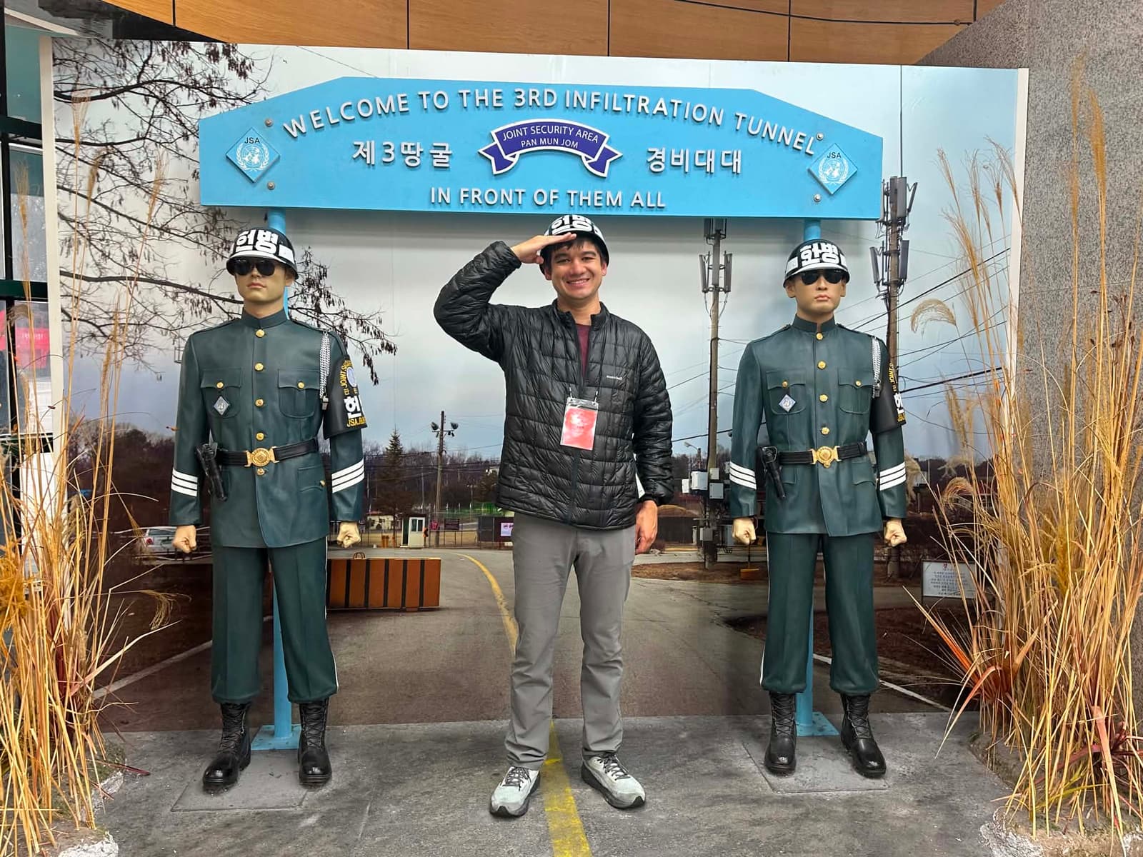 Anthony saluting between two mannequin Korean military police at the entrance to the 3rd Infiltration Tunnel, with a Joint Security Area sign overhead